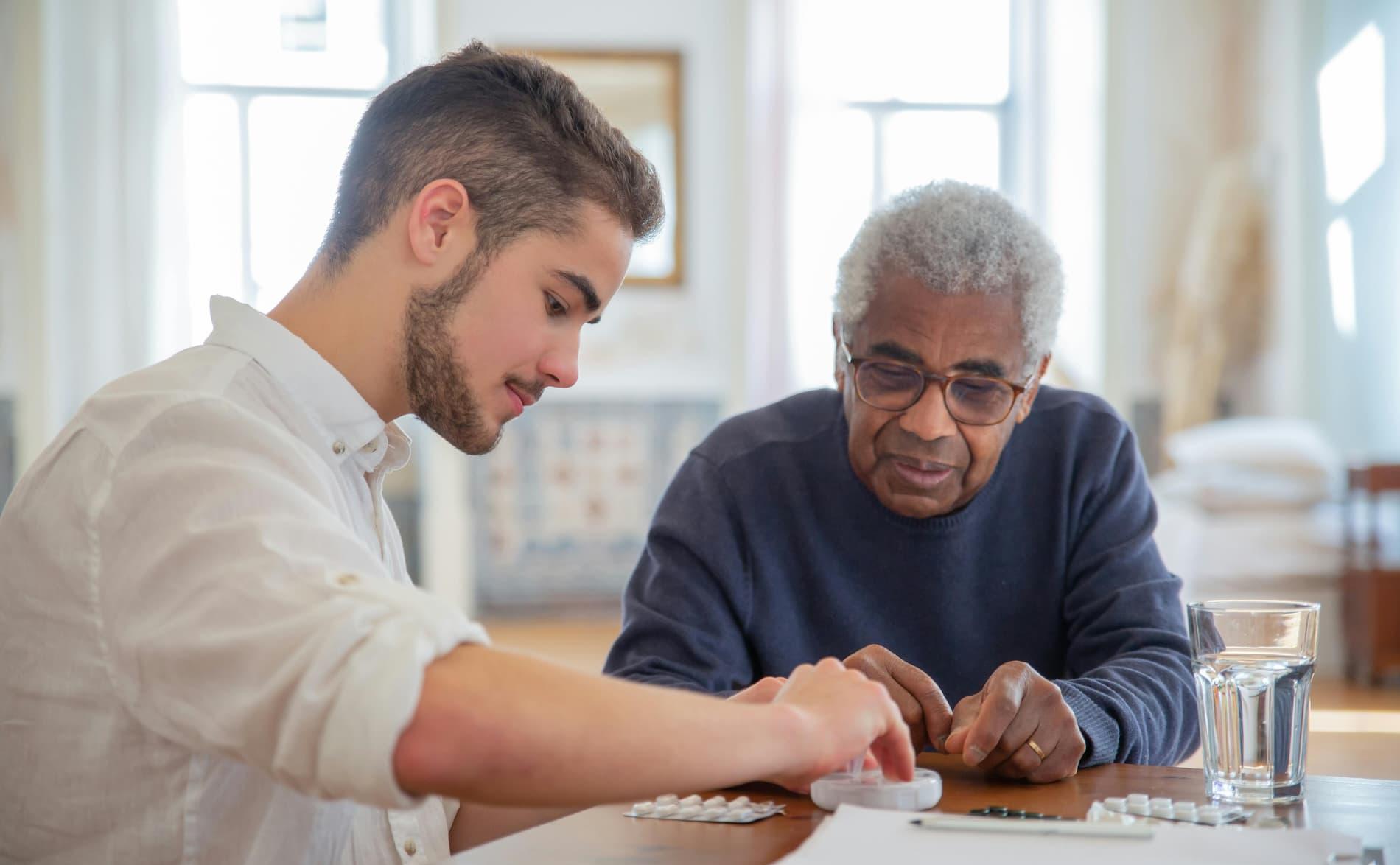 Young man helping older man with pills in his home