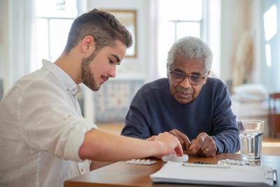 Young man helping older man with pills in his home