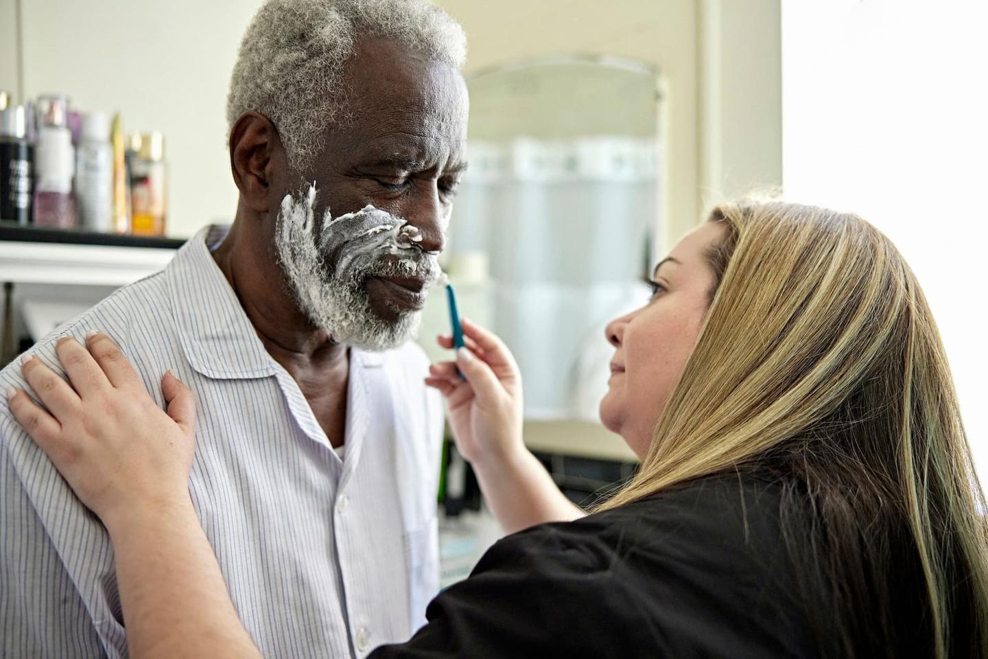 A woman assisting an older man shaving